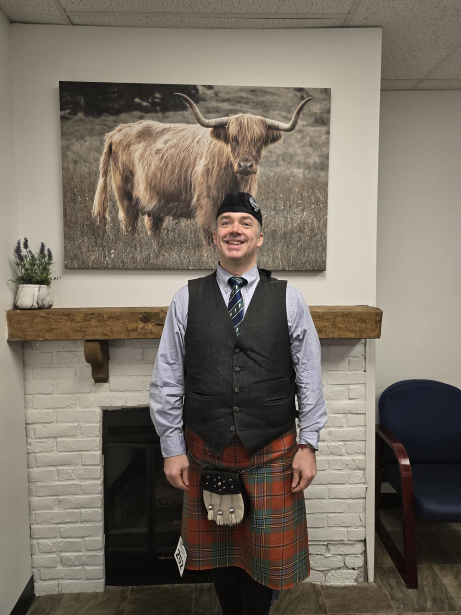 Cristopher Rodriguez posing in front of painting of a Scottish cow at the Rose and Shamrock bagpipe competition.